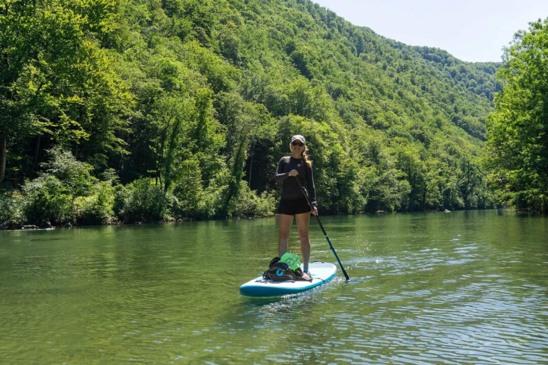 Women paddleboarding on a SUP board on a river in Slovenia, surrounded by green forest and hills