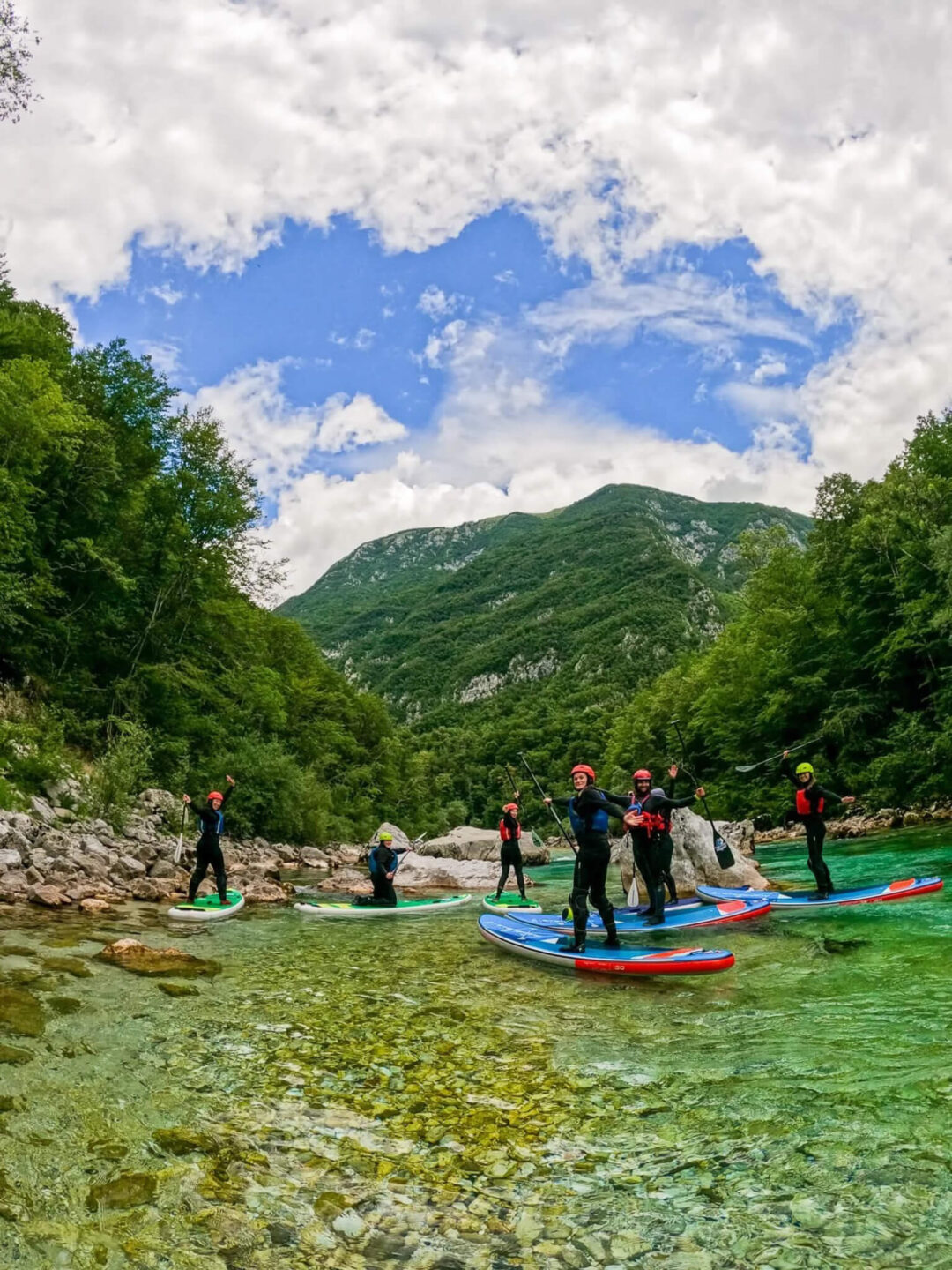 Women whitewater SUP paddling on a clear river in Slovenia, with green mountains and blue sky behind them