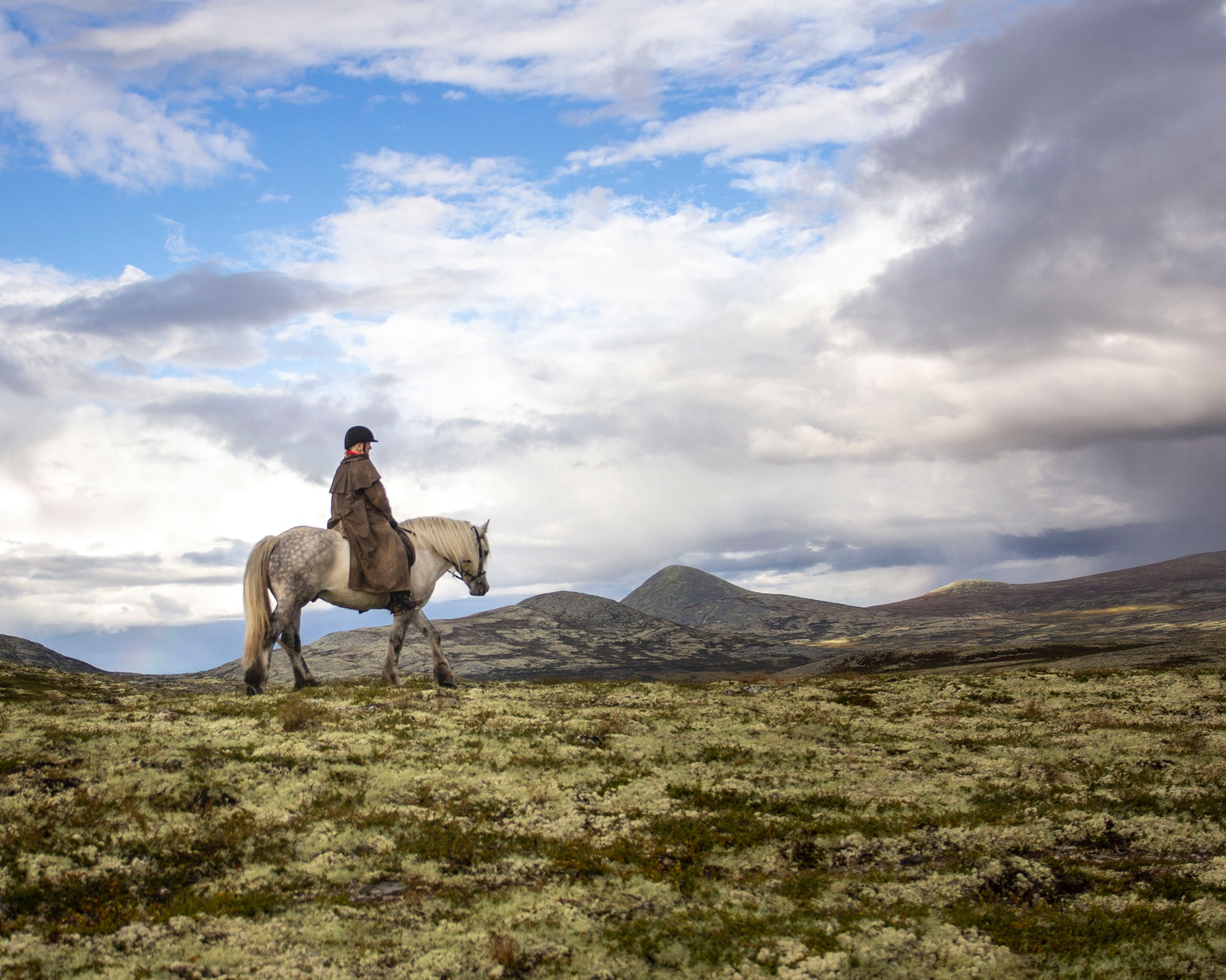 Woman horse rider on horseback in a mountainous landscape under a cloudy sky