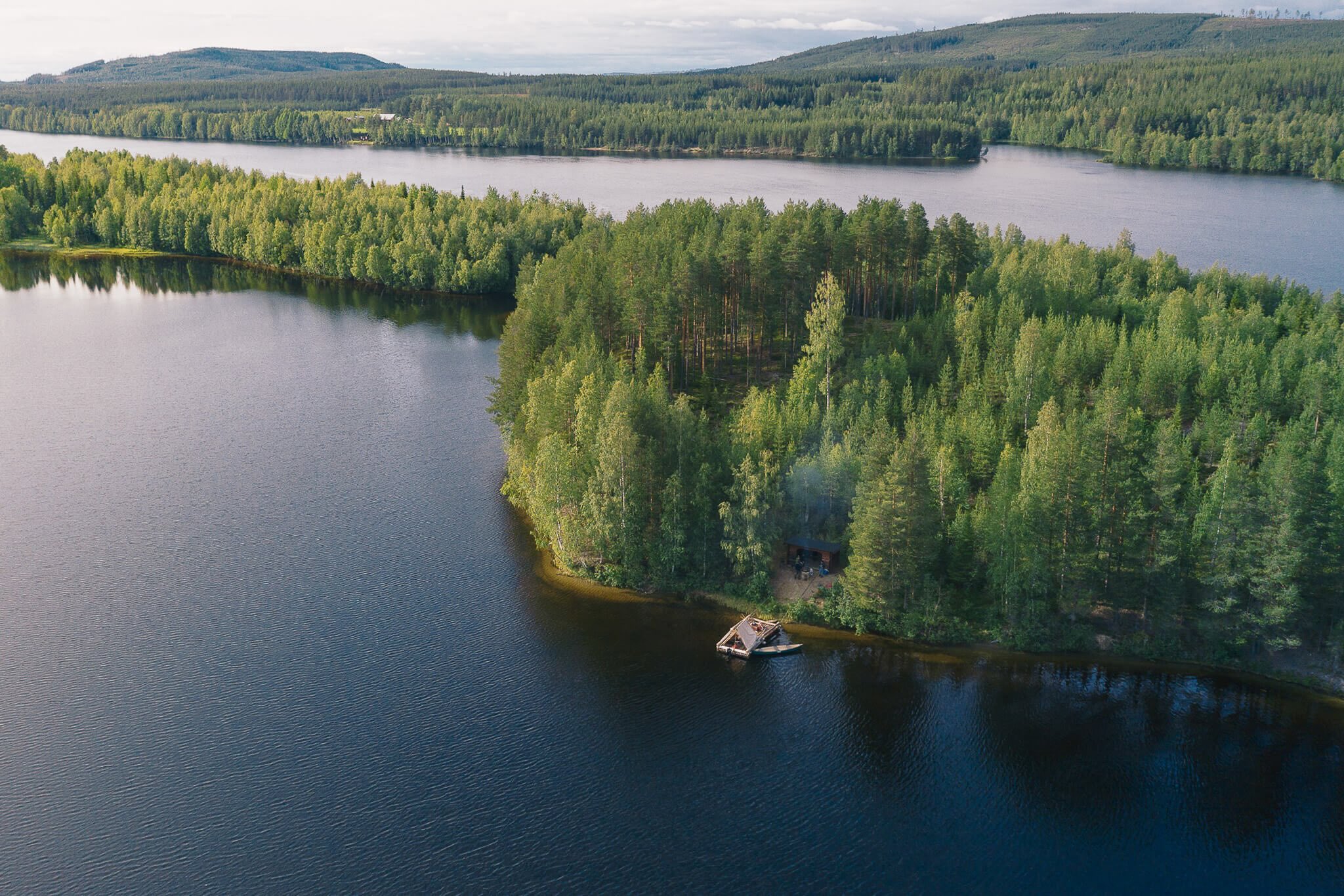 Aerial view of a forest lake with a small cabin by the shore in Swedish Lapland, Sweden