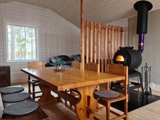 Women’s wilderness cabin interior with wooden tables and a black wood-burning stove, by a window in Swedish Lapland