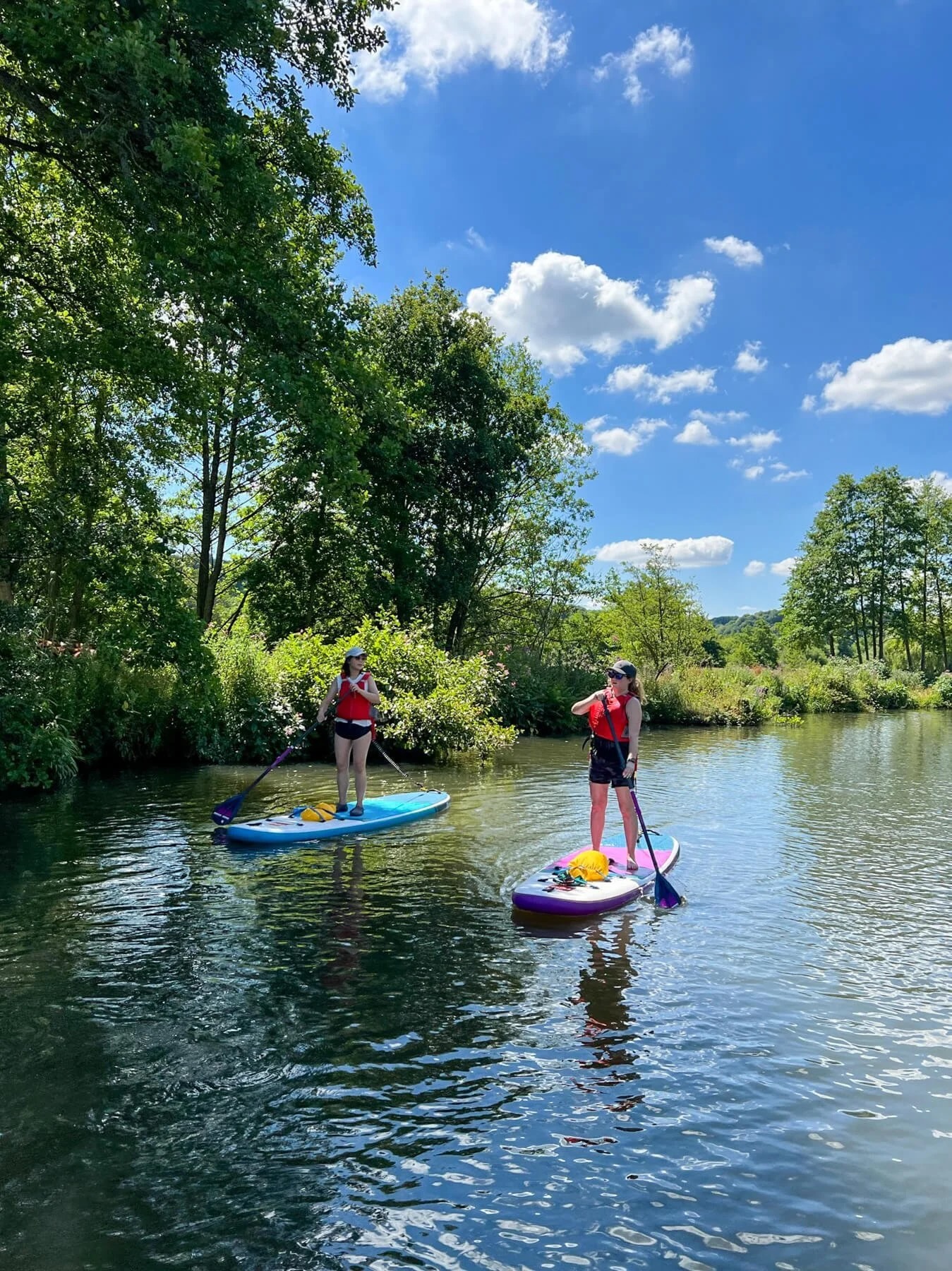 Women beginner paddleboarding on a calm river surrounded by trees and blue sky