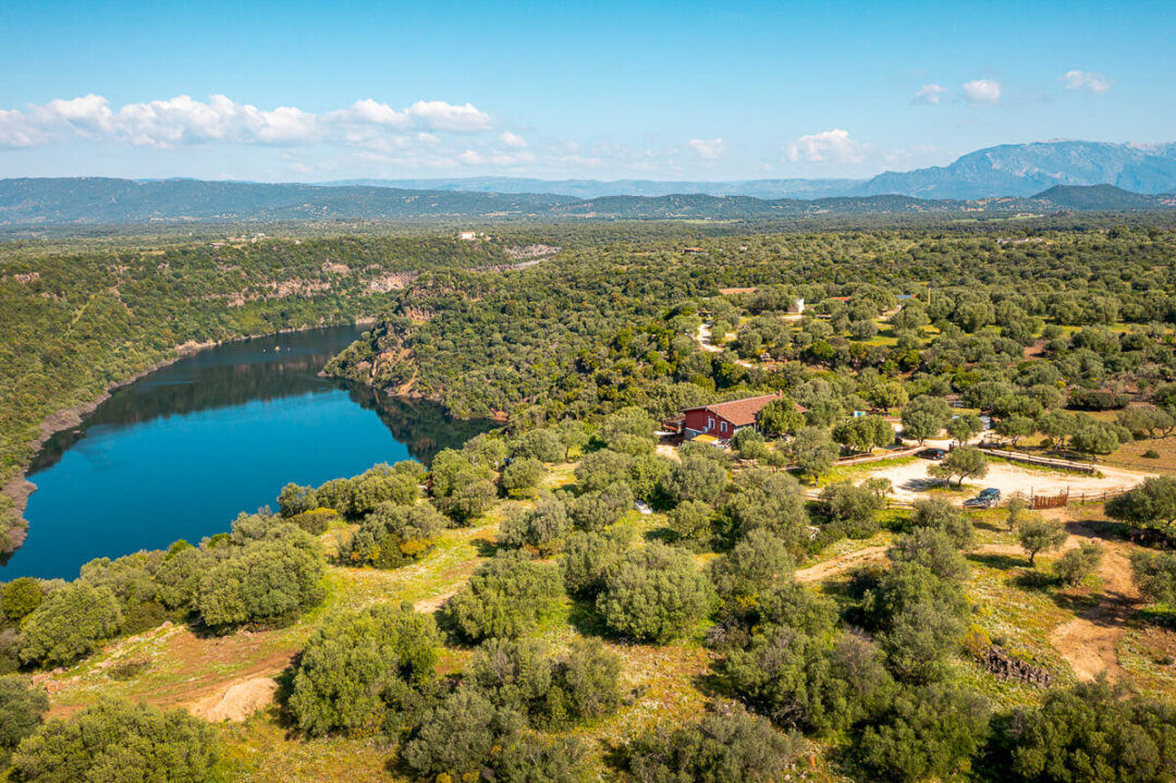 Aerial view of Sardinia’s east coast landscape with river, fields, and a rural building.