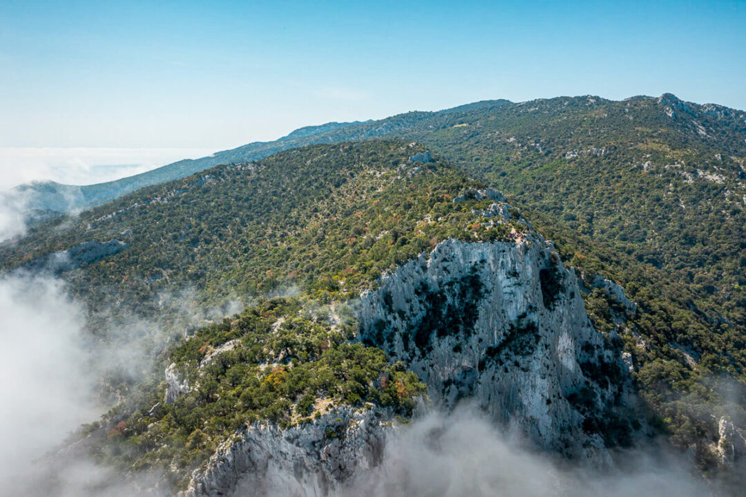 Aerial view of hikers on Sardinia’s east coast, with mist over green mountains and forested hills