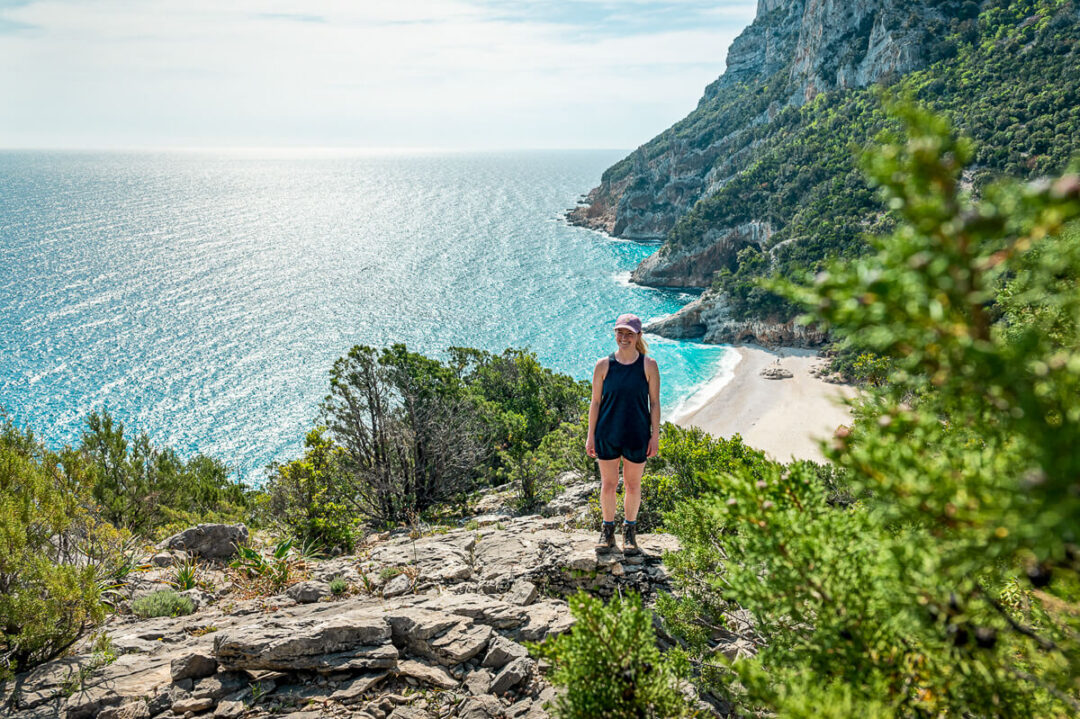 Woman hiking along Sardinia’s east coast overlooking a secluded beach and sea cliffs