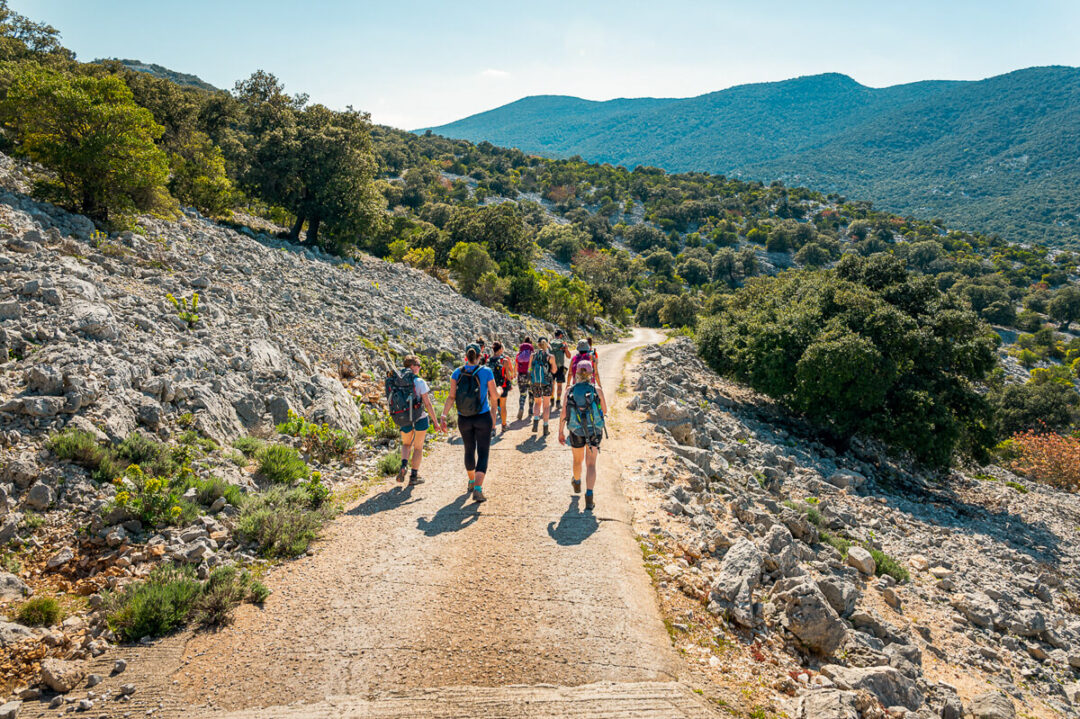 Women hiking along a rocky trail through green Mediterranean hills in Sardinia