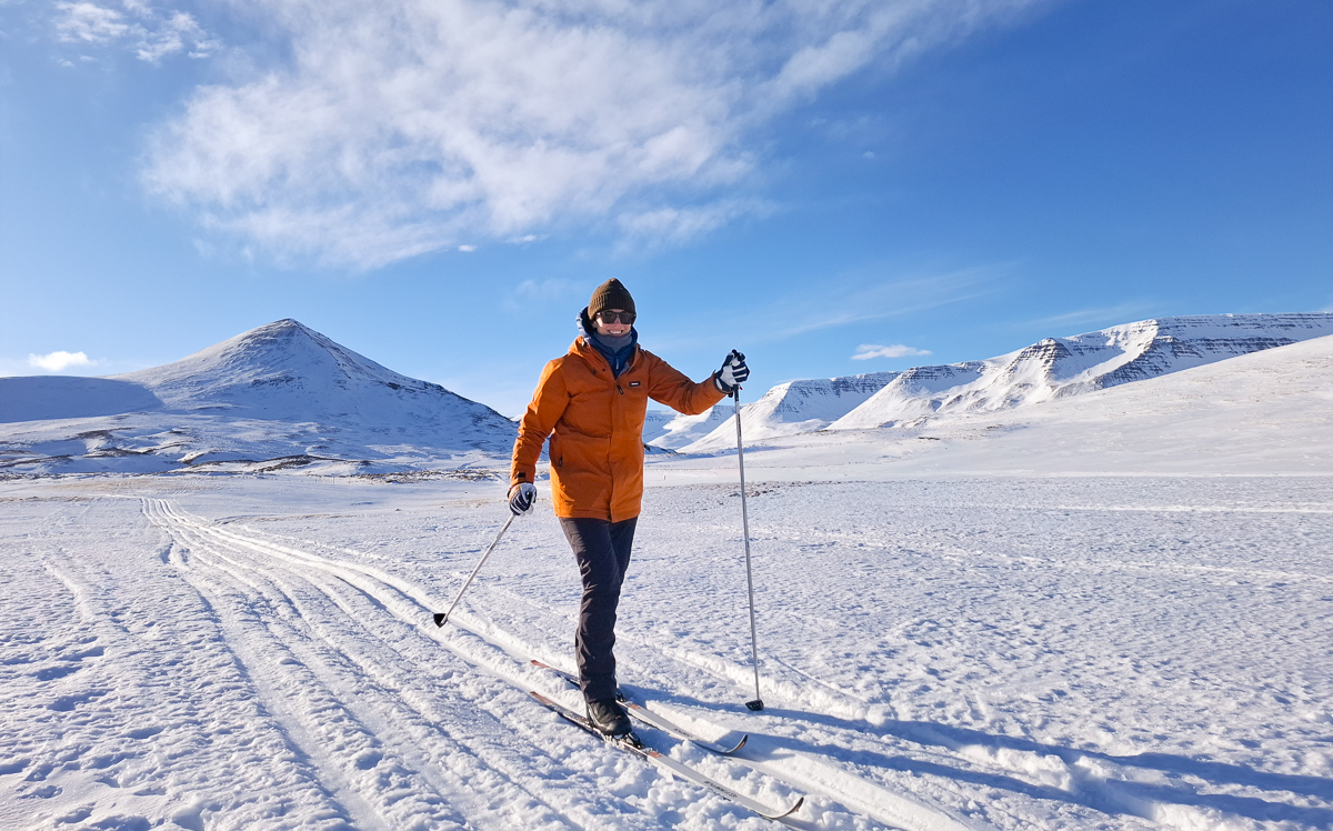 Woman cross-country skiing on snowy tracks in a mountain landscape under a clear blue sky