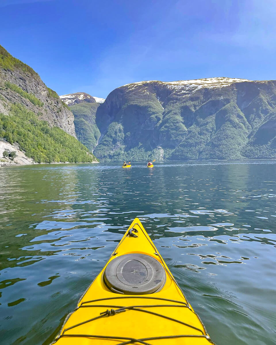 Woman kayaking on a calm fjord in Jotunheimen National Park, surrounded by steep green mountains and snow-dusted peaks.