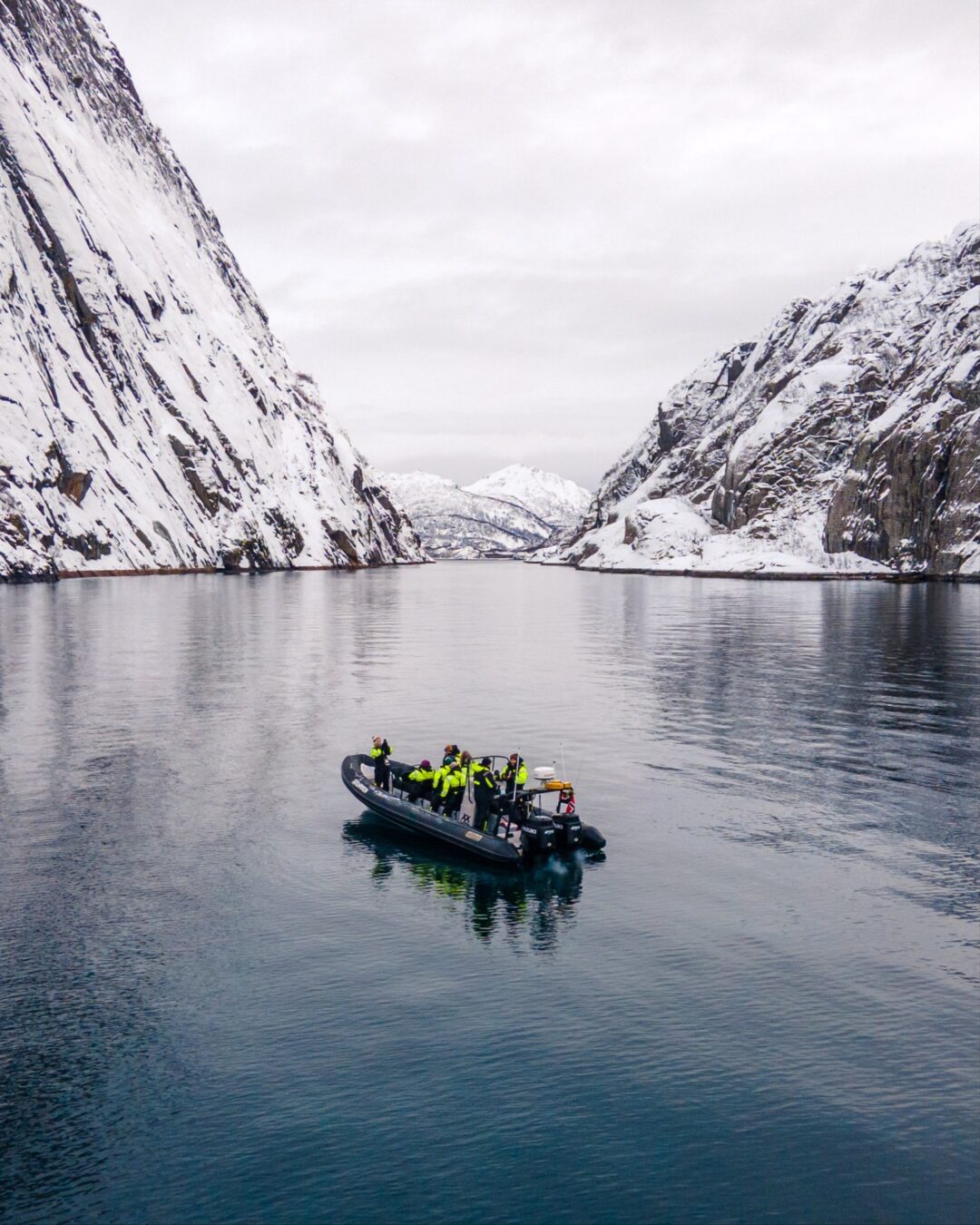 Boat in calm snowy fjord with mountains, Lofoten (Norway)