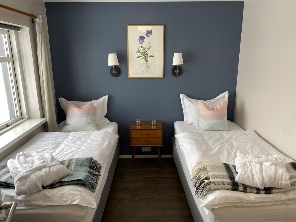 Two neatly made single beds in a bright double bedroom with bedside tables and lamps