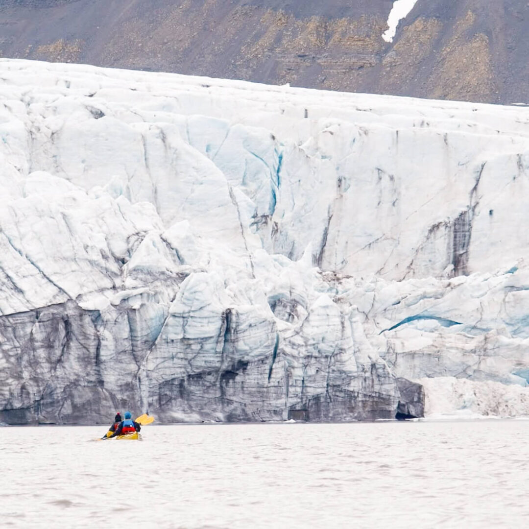 Women kayaking in calm waters beside a glacier in Svalbard, Arctic Wilderness summer expedition