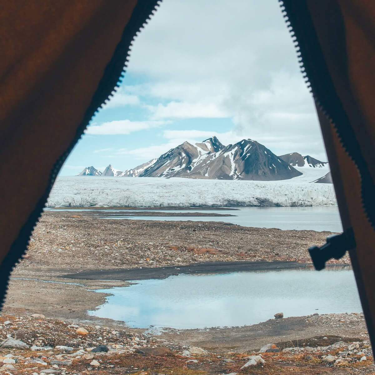 View of snowy mountains and glacier in Svalbard through a tent opening during an Arctic wilderness expedition