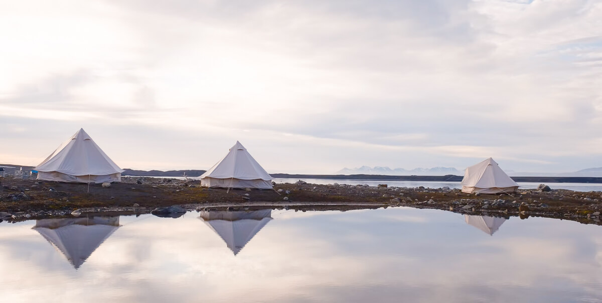 White camping tents reflected in still water on an Arctic wilderness campsite in Svalbard