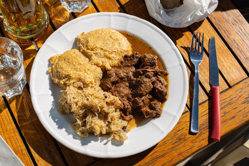 Plate of meat and potatoes on a wooden table with cutlery and water glasses, shared meal at a mountain hut.