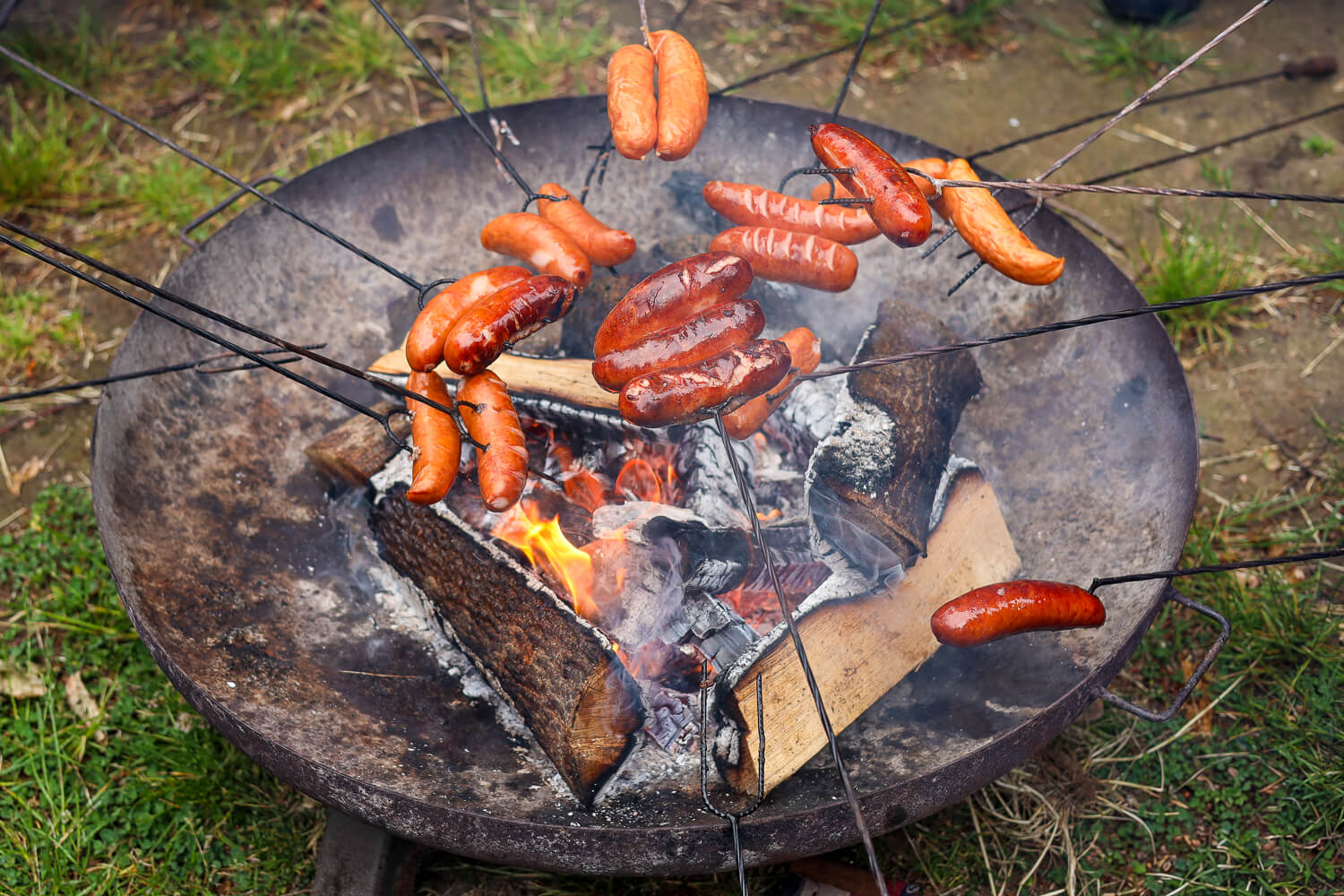 Sausages cooking over an open campfire barbecue on a metal grill outdoors