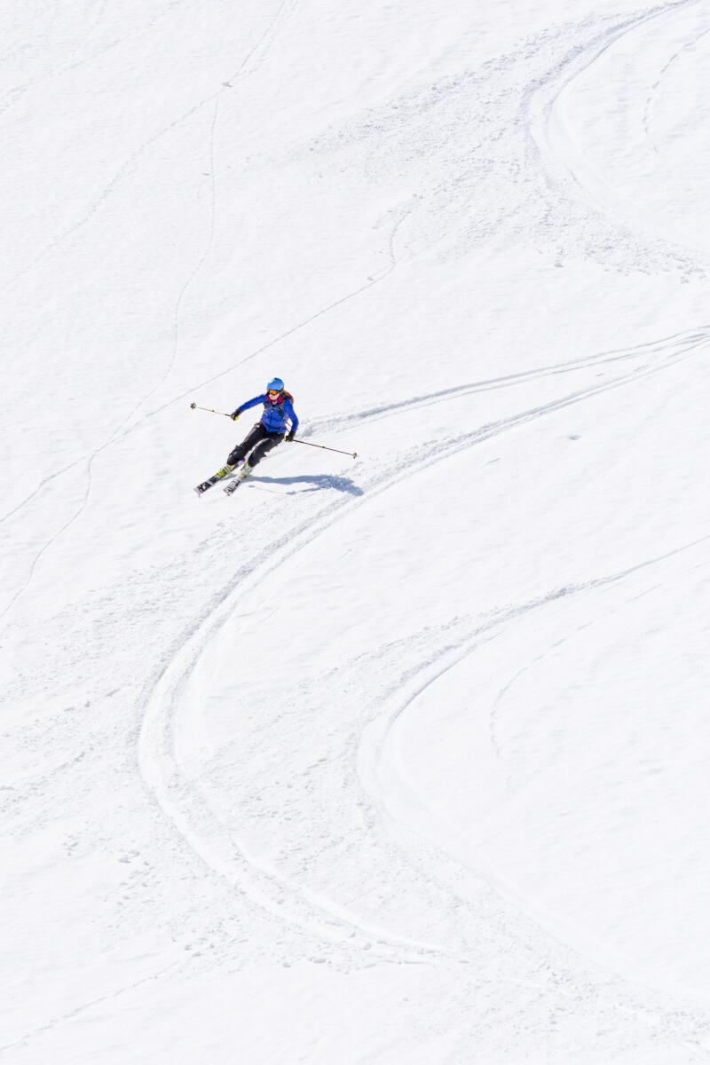 Woman ski touring downhill on snowy slopes with skis and poles