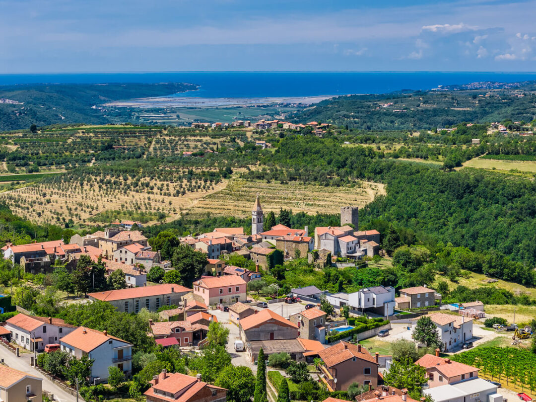 Aerial view of a hilltop coastal town overlooking a sandy beach and blue sea.