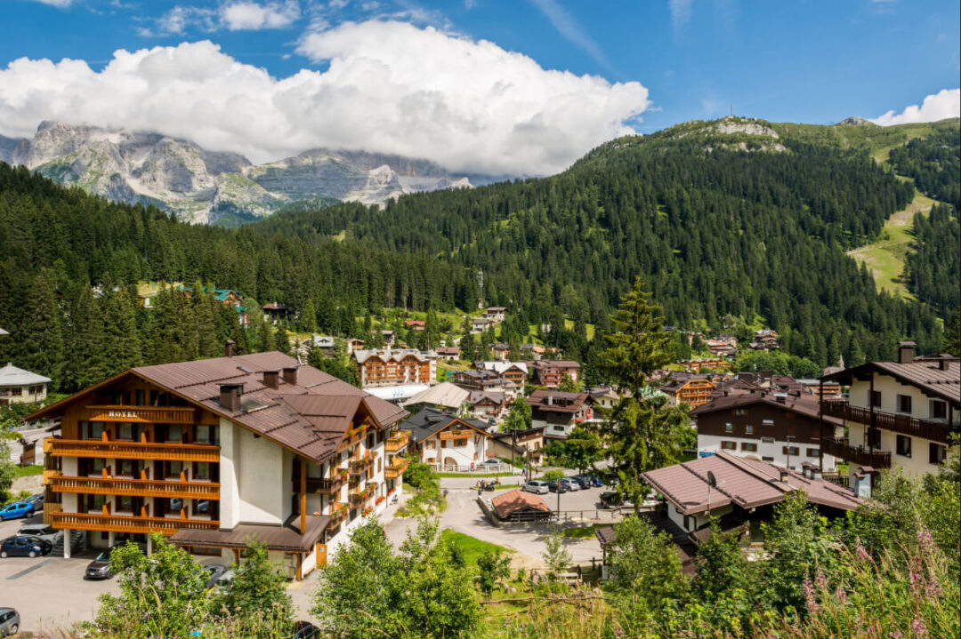 Alpine village in the Dolomites with mountain peaks and forested valley under a blue sky