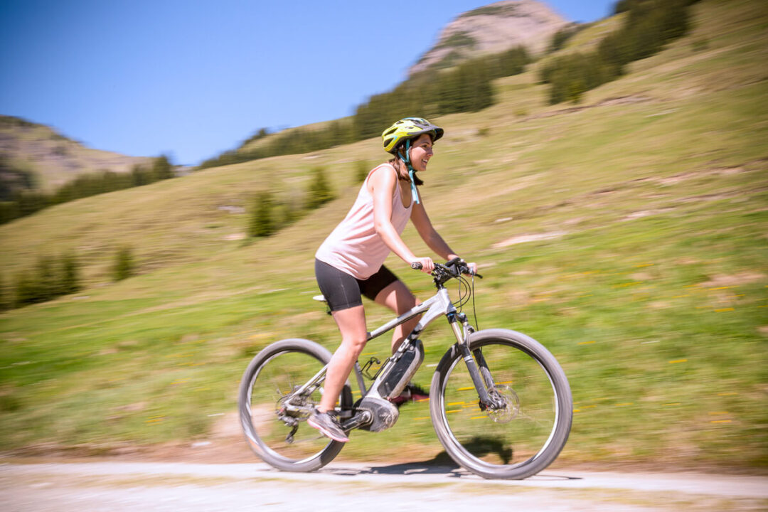 Woman mountain biking on a road through green hills, wearing a helmet and sportswear.