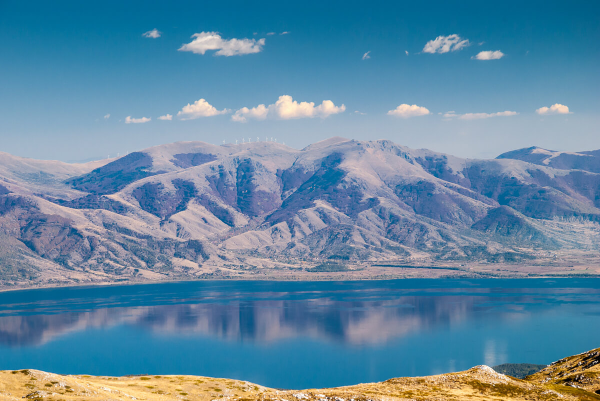 Lake Ohrid in North Macedonia, calm blue water with mountain ranges and their reflections under a cloudy sky