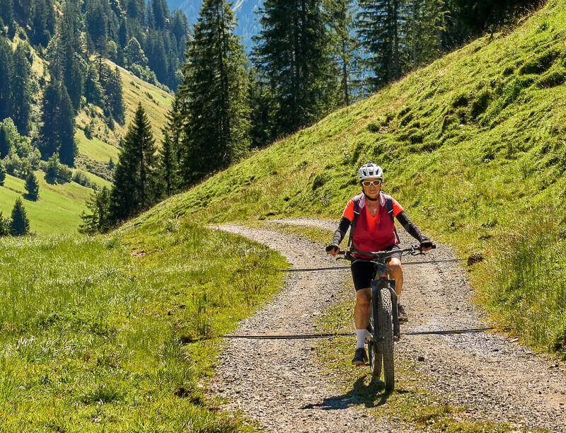 Woman mountain biking on a gravel path through an alpine forest valley