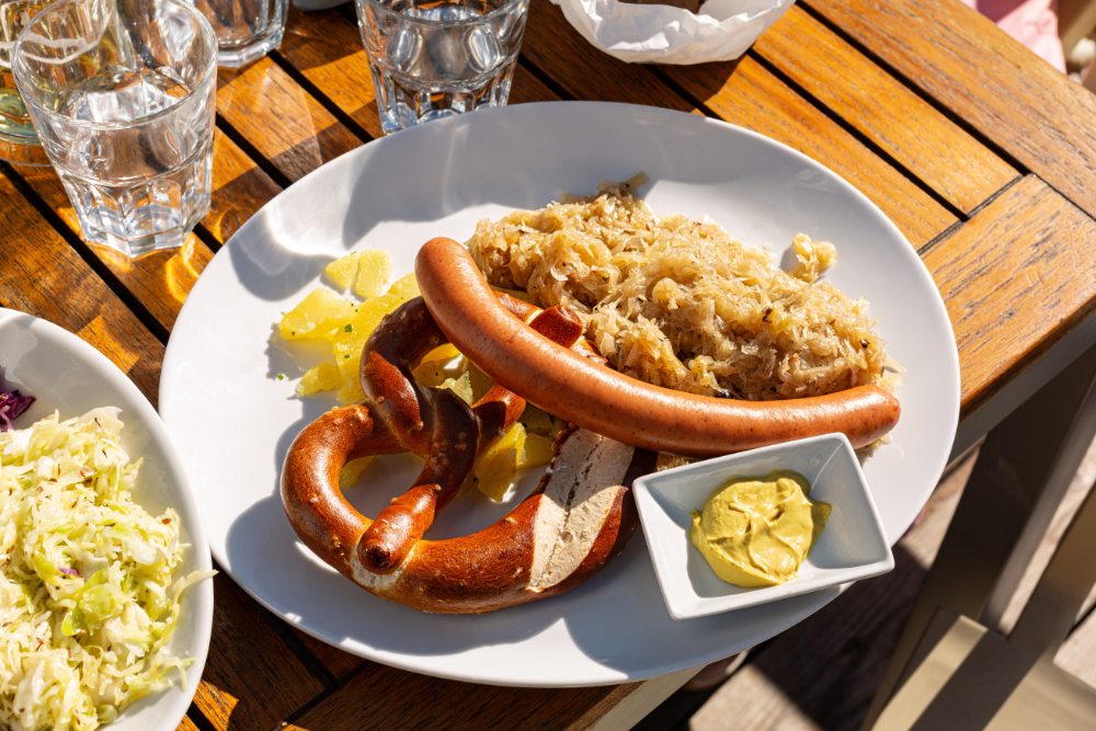 Sausages and sauerkraut on a plate with mustard on the side, served on a wooden table with glasses