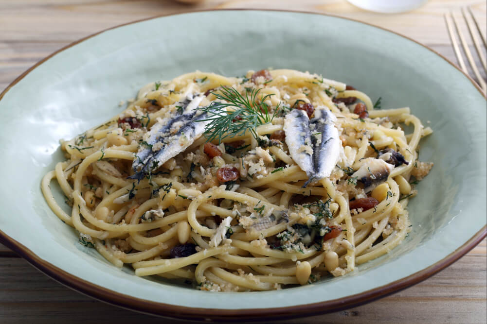 Spaghetti with anchovies, herbs and pine nuts in a green bowl, served on a wooden table