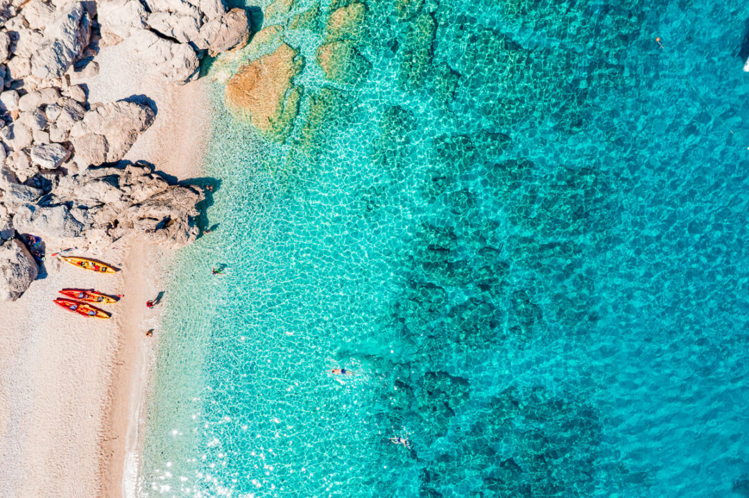 Kayaking near a rocky beach with bright turquoise sea and clear waves