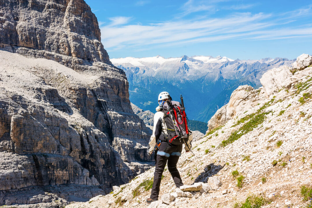 Woman on a via ferrata route in the Dolomites, climbing rocky trail with mountains in the background