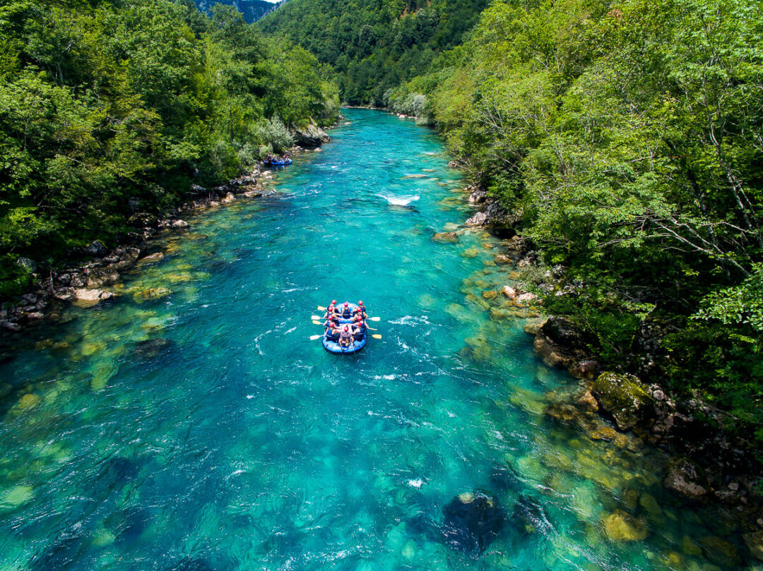 Rafting on a clear turquoise river through a lush forested valley with mountains in the distance