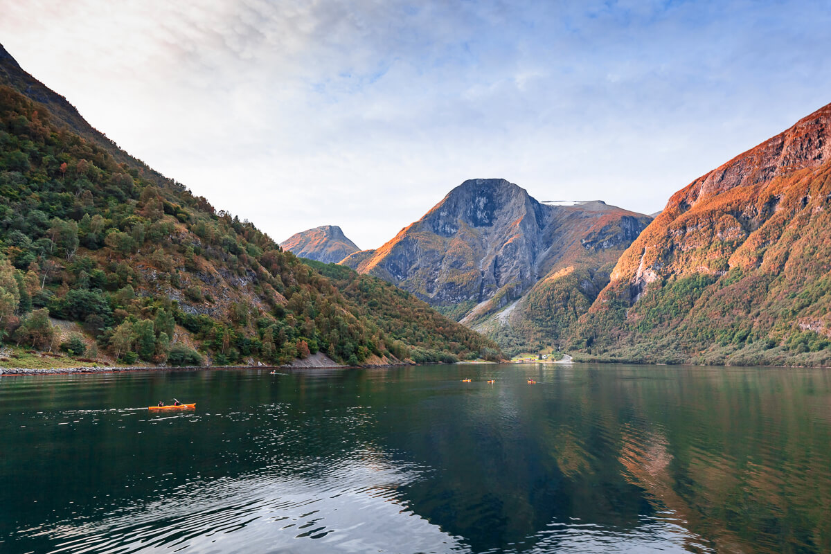 Orange kayak on still mountain lake with towering cliffs and autumn colours