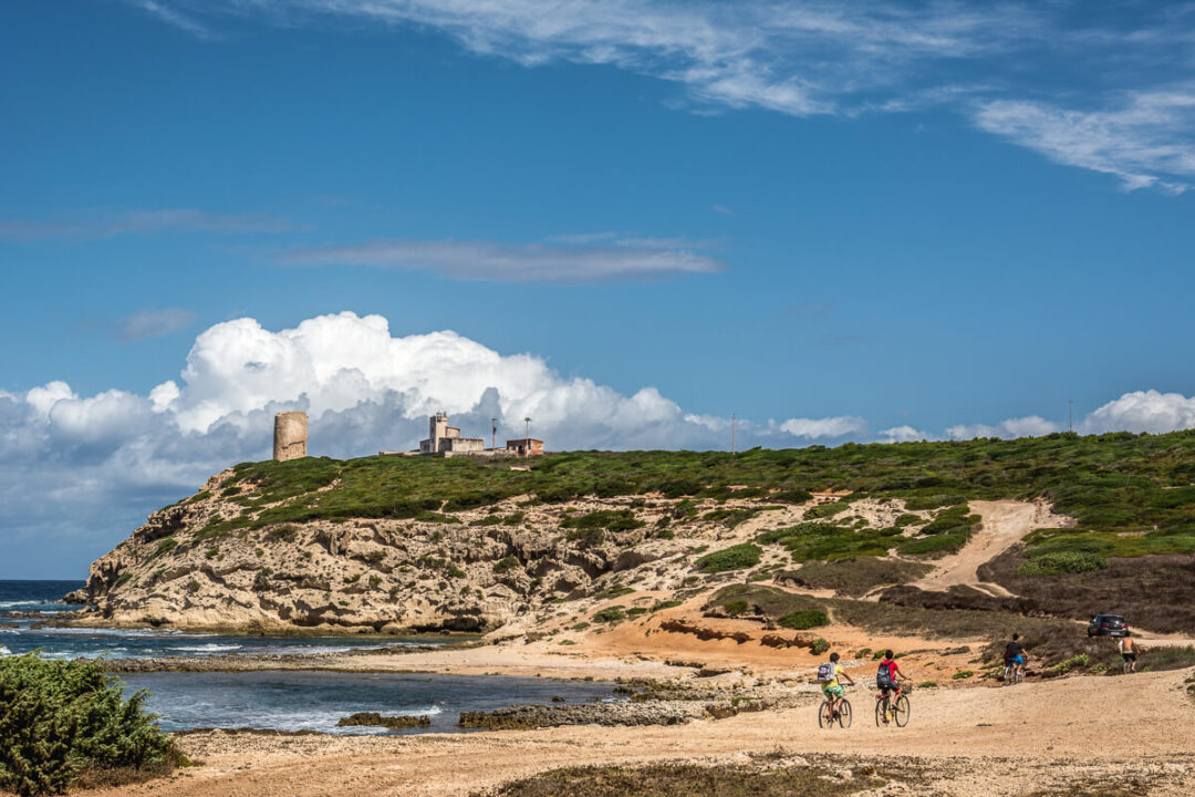 Cyclists ride along a coastal track with sea views near hilltop ruins in East Sardinia