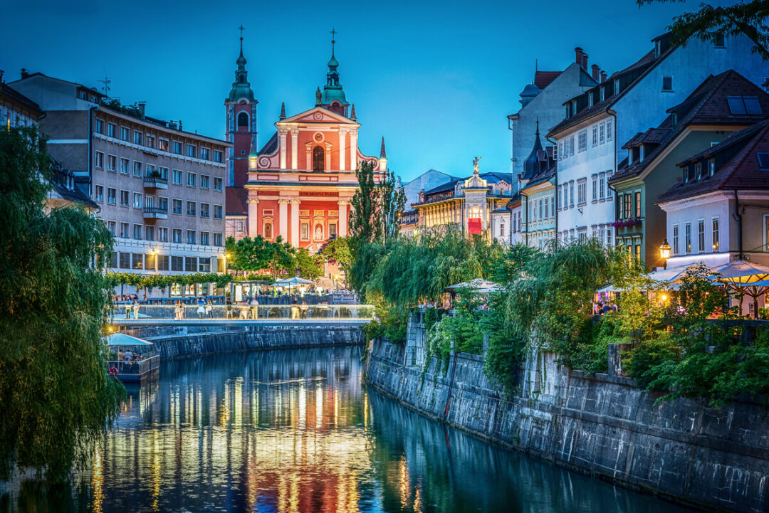 Historic church and riverfront buildings at dusk in an European town, with reflections on the water