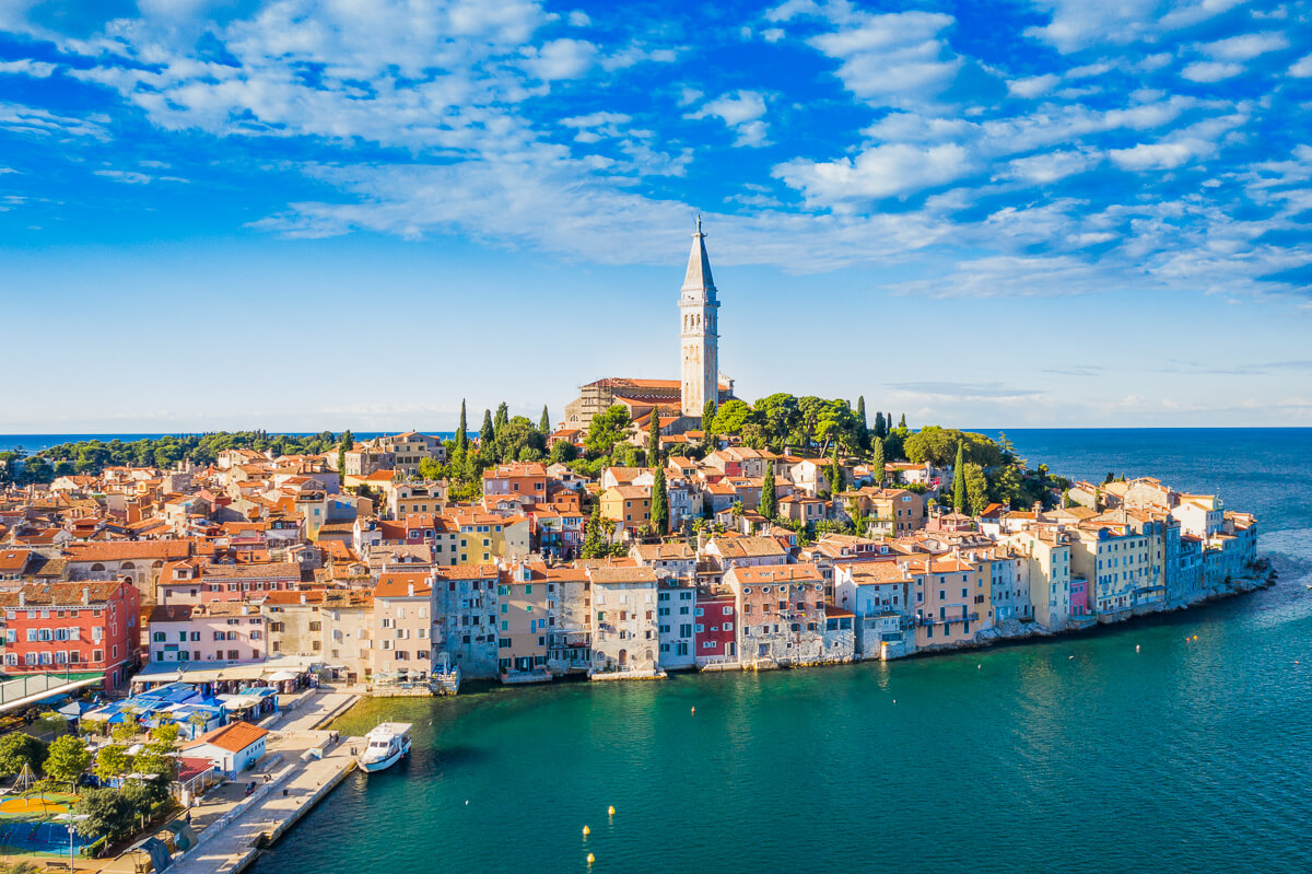 Aerial view of a coastal town with a tall church tower and colourful harbour buildings by turquoise sea