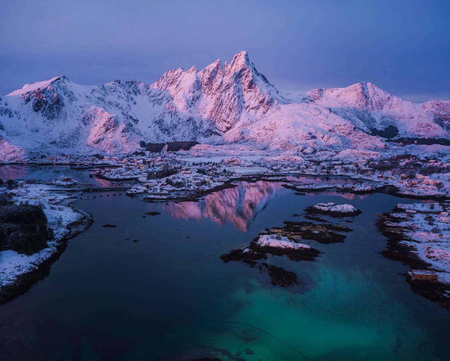 Snowy mountain fjord at dusk with icy shoreline and clear blue water