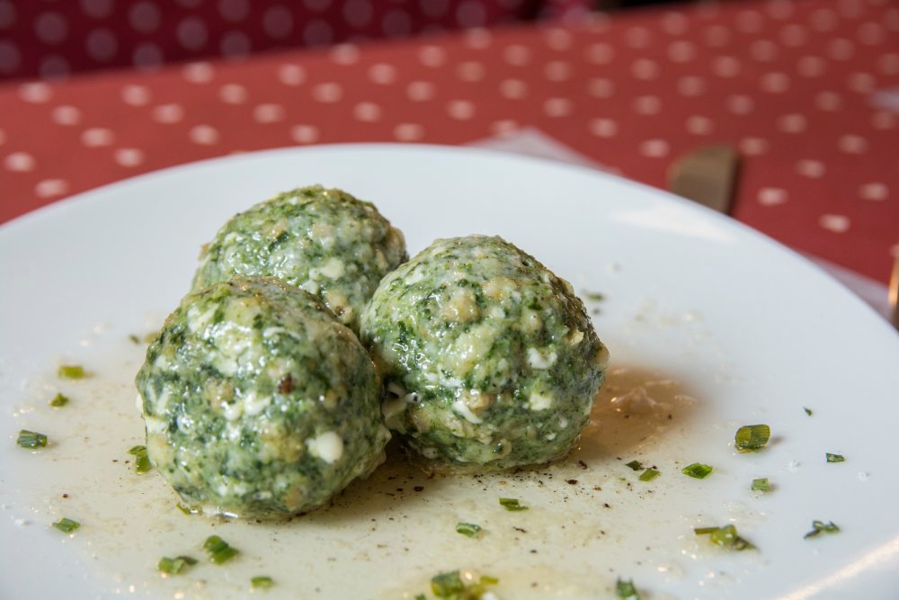 Green herb dumplings on a white plate with herb crumbs, on a red tablecloth background.