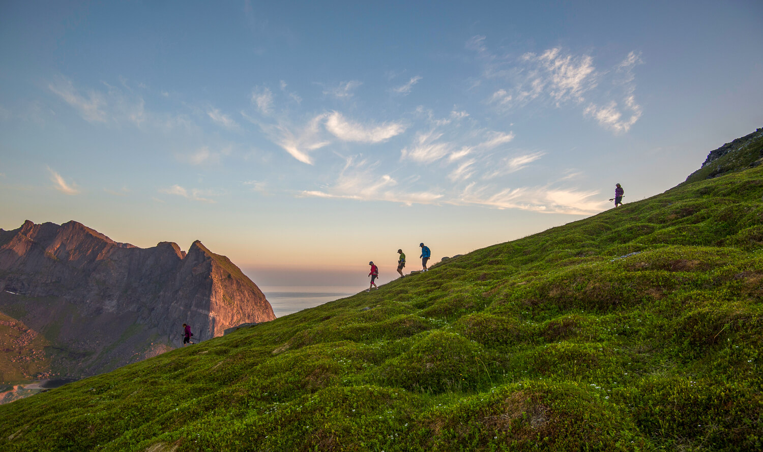 Women hiking along a grassy mountainside at sunset over dramatic coastal scenery