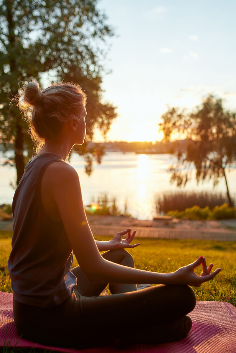 Woman meditating in yoga on a lakeside mat at sunset, Lake Ohrid, North Macedonia.