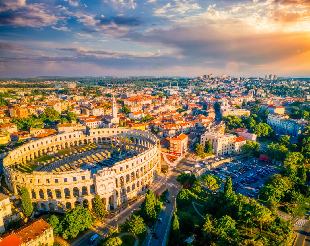 Aerial view of the Colosseum in Rome, Italy at sunset, with city streets and buildings below