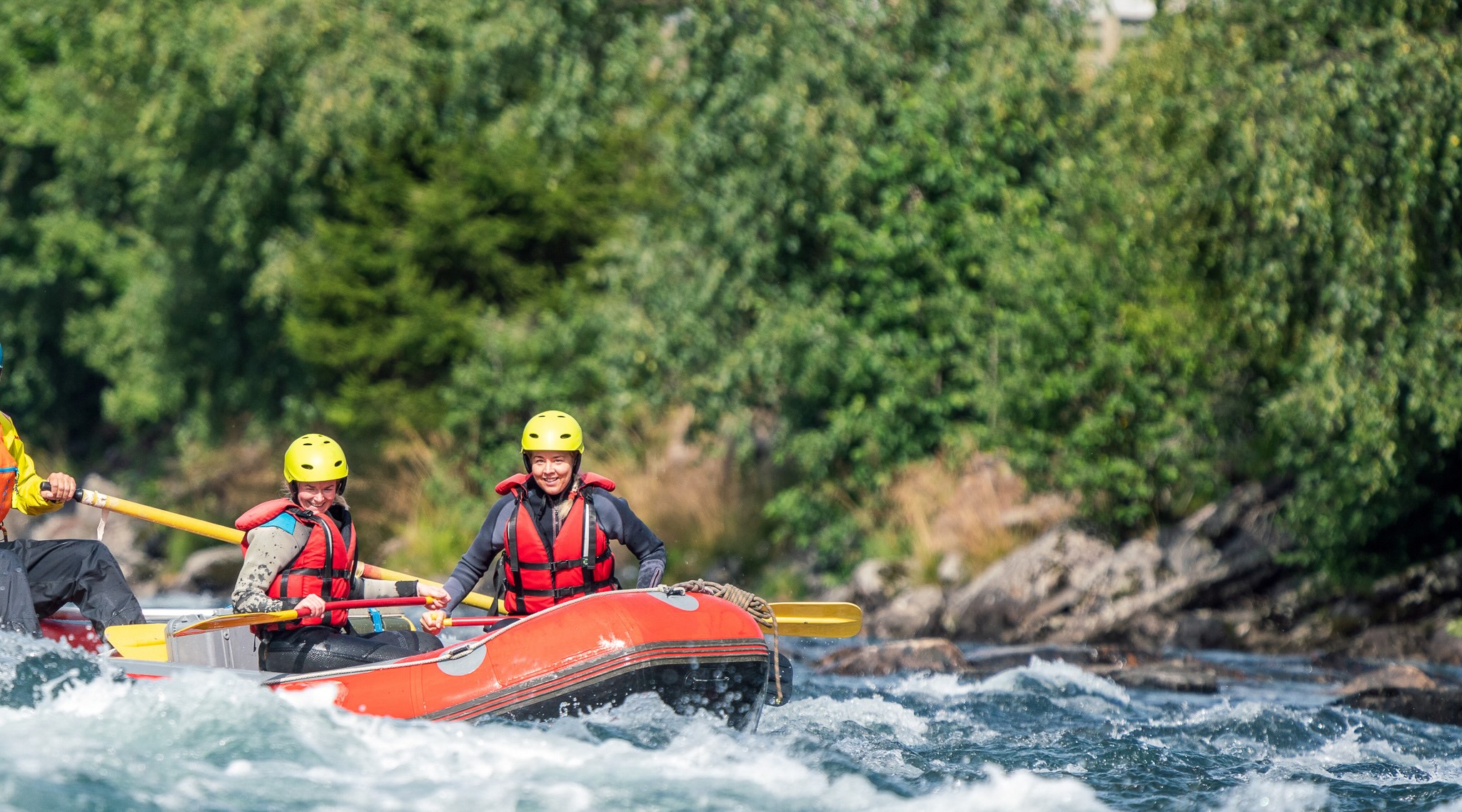 Women in helmets paddling an inflatable raft on whitewater rapids