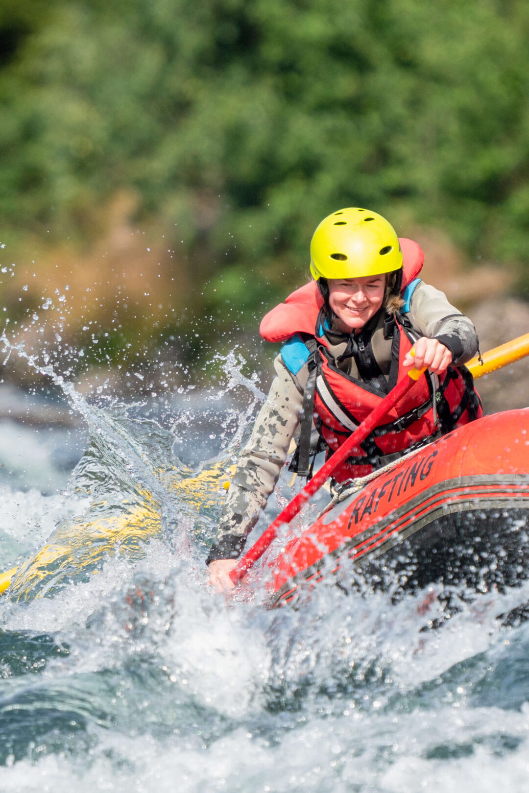 Women kayaking in white-water rapids on a river, wearing a yellow helmet and red life jacket