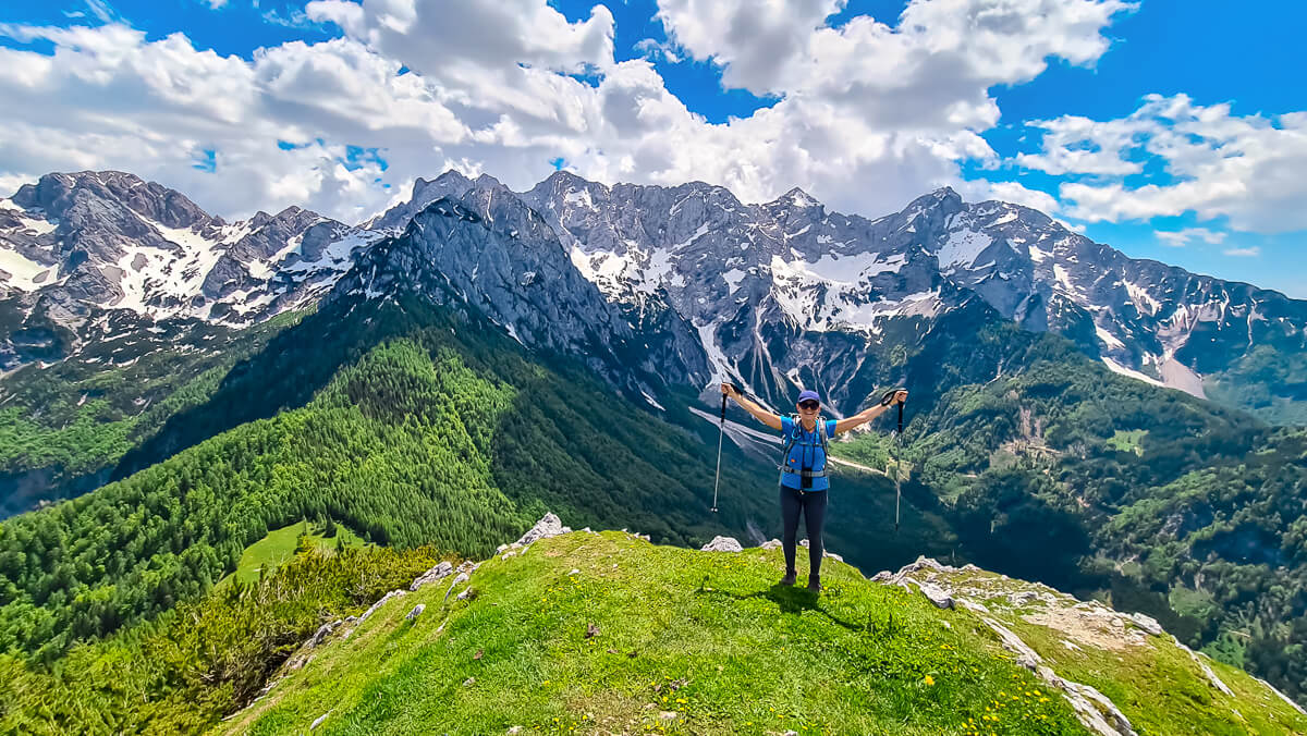 Woman hiking on a grassy ridge above the Alps, overlooking a mountain valley and snow-capped peaks