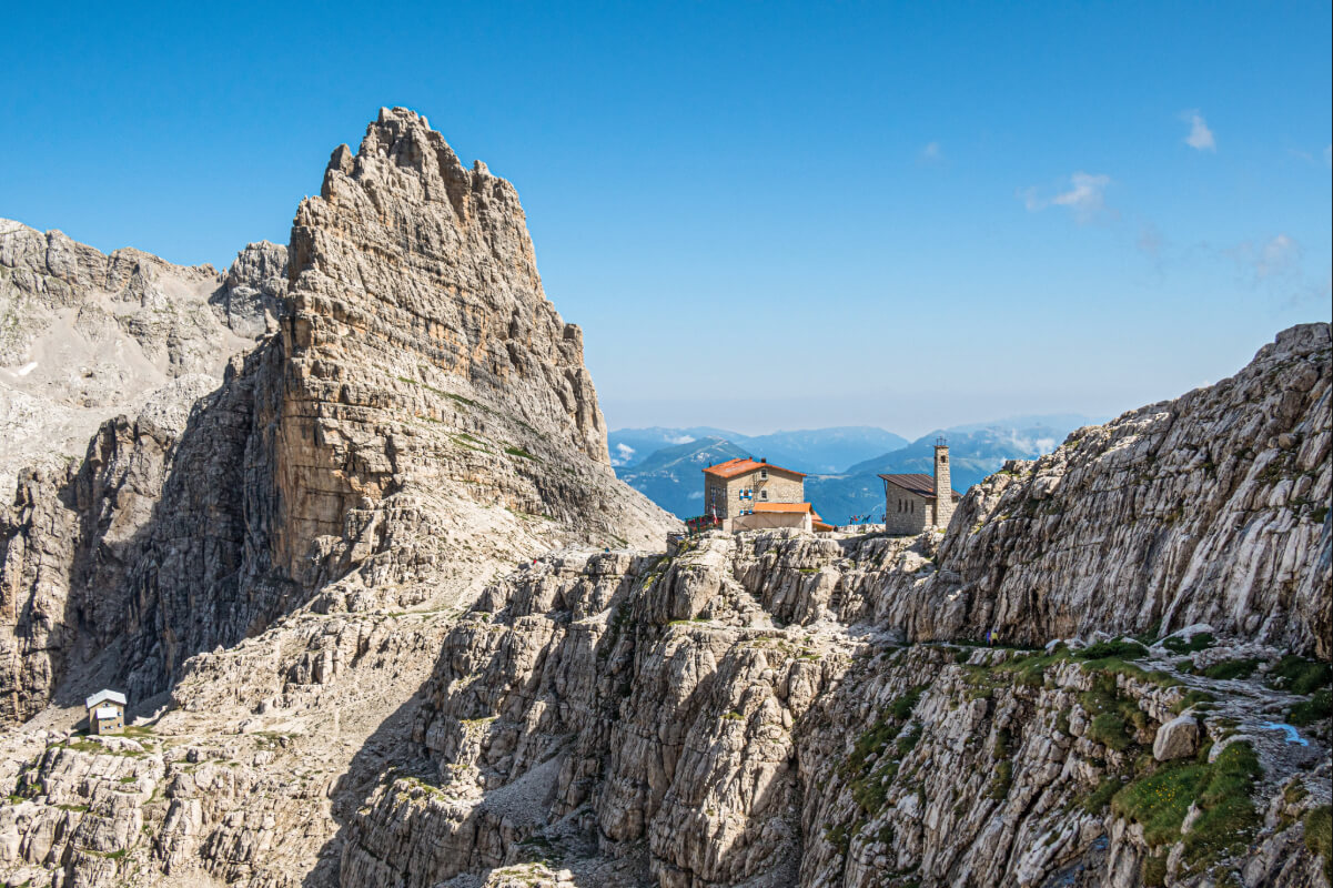 Via ferrata route in the Dolomites above a rocky mountain hut on the trail, with steep cliffs and blue sky