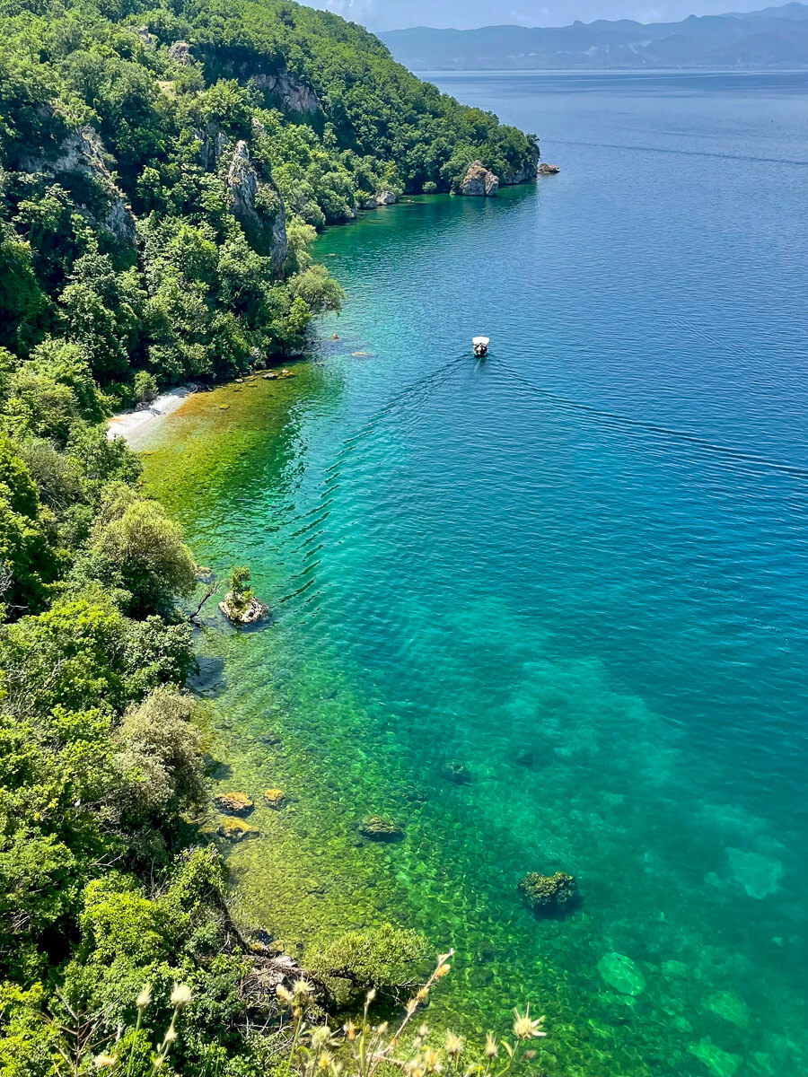 Turquoise Lake Ohrid shoreline with a small boat and forested cliffs in North Macedonia.