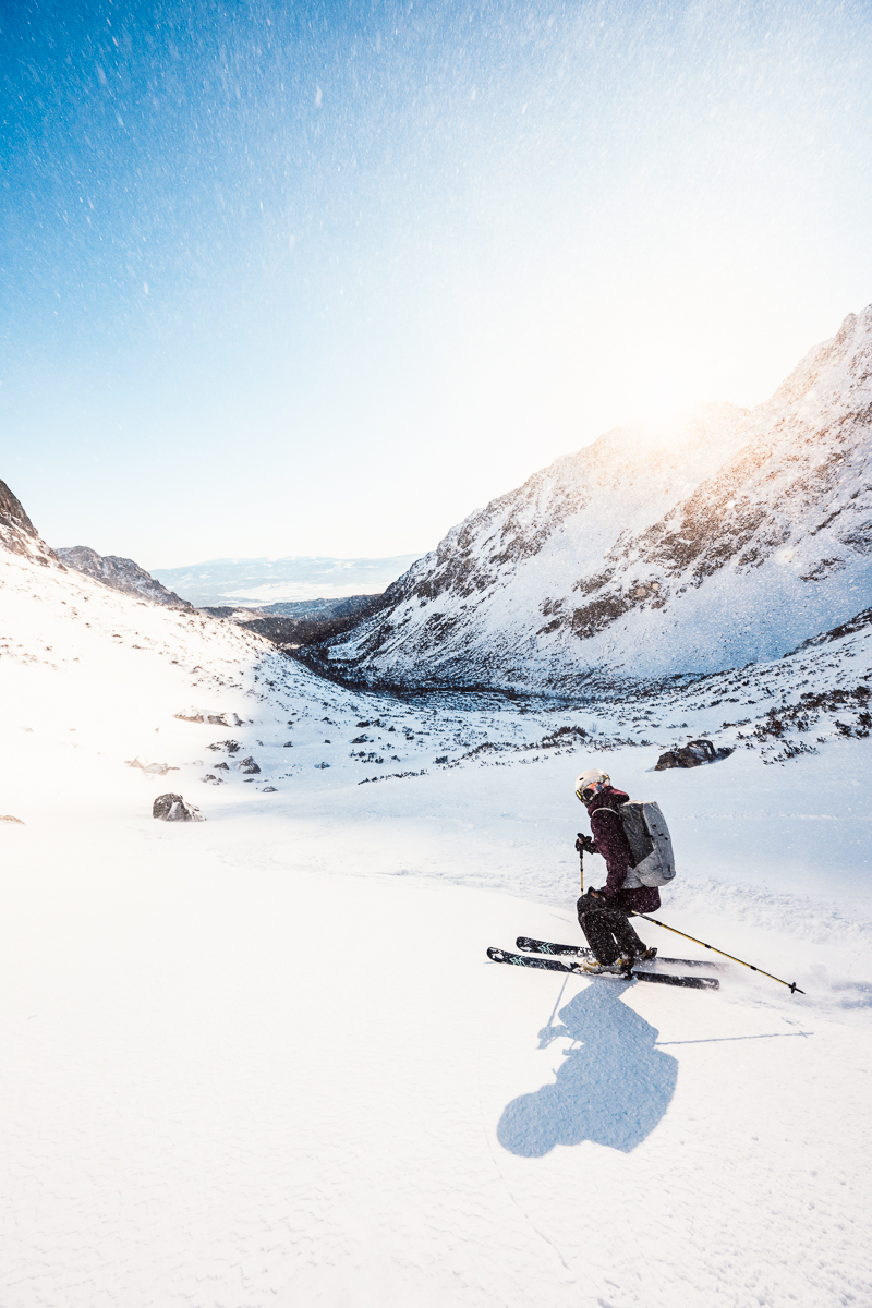 Skier doing ski touring across a snowy mountain valley under a bright winter sky