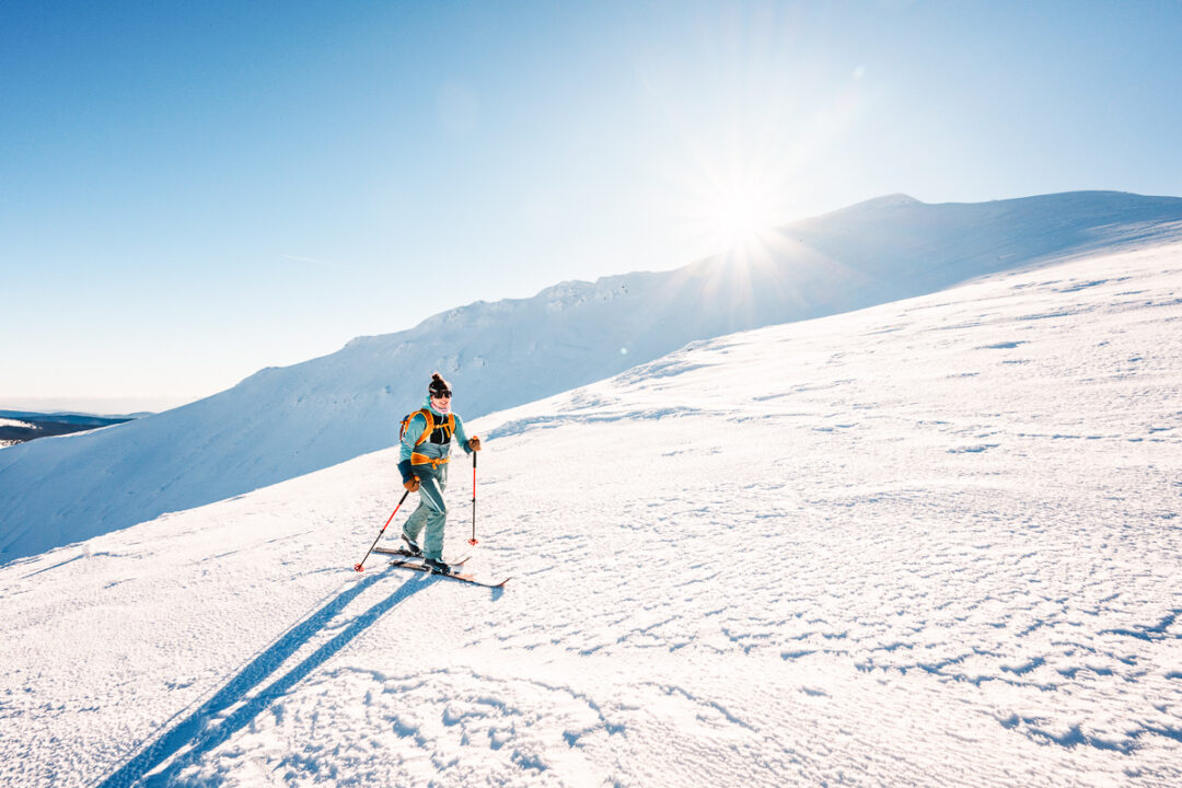 Woman ski touring on a snow-covered mountain slope under bright sunshine
