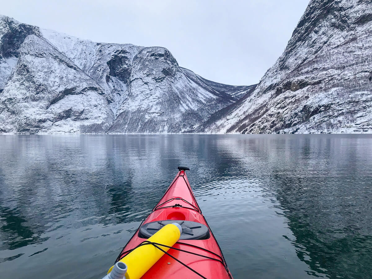 Red kayak paddling on a fjord with snow-covered mountains in Norway