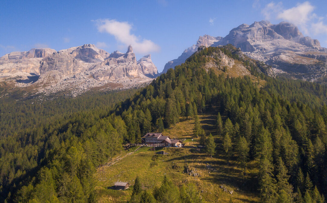 Dolomites mountain valley in Italy with alpine cabins and forested slopes under a clear sky