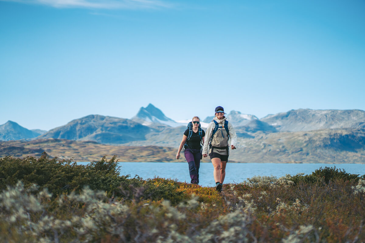 Women hiking across a mountain landscape with a lake and peaks in the background