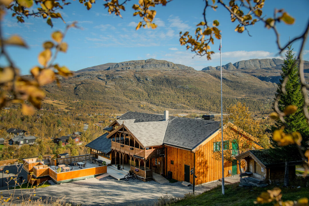 Scenic view of a wooden lodge and mountain valley village in Jotunheimen, Norway, with autumn trees.